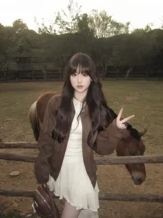 Woman in a white dress and brown jacket posing with a horse outdoors