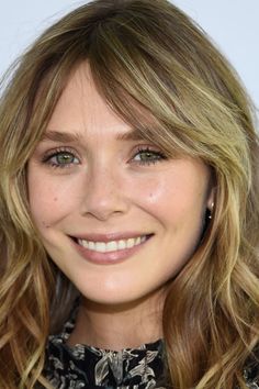 Close up portrait of a smiling woman with blonde wavy hair and green eyes