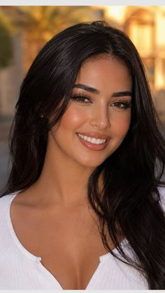 Woman with long dark hair smiling in a white top with cleavage