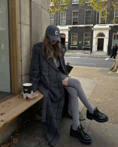 Woman in a plaid coat and baseball cap sitting on a bench outdoors