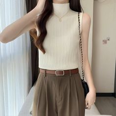Woman in a white sleeveless turtleneck top and brown pants with a belt