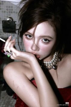 Woman with dark hair and a pearl necklace in a red dress, holding a cigarette