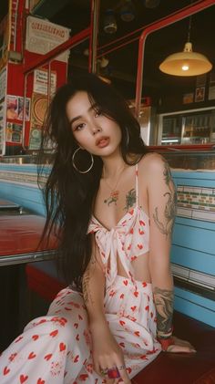 Woman with long dark hair and tattoos wearing a heart-patterned crop top in a diner