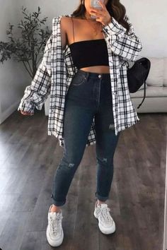 Woman in a plaid shirt, crop top, and ripped jeans taking a mirror selfie
