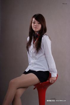 Woman with long hair wearing a white shirt and black skirt, sitting on a red stool