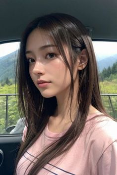 Woman with long dark hair in a pink t-shirt inside a car with mountains in the background