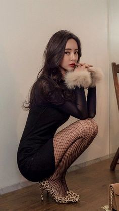 Woman in a black dress and fishnet stockings squatting indoors