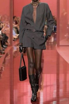 Model in a dark grey outfit with a deep V-neck on a red runway