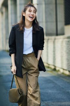 Woman in a black blazer and khaki pants laughing outdoors