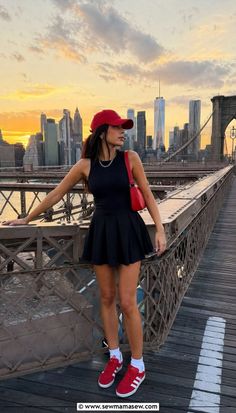 Woman in a black dress and red cap on the Brooklyn Bridge at sunset
