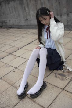 Young woman in a school uniform and white tights sitting on tiled ground