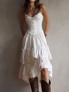 Woman in a white corset dress and cowboy boots leaning against a wall