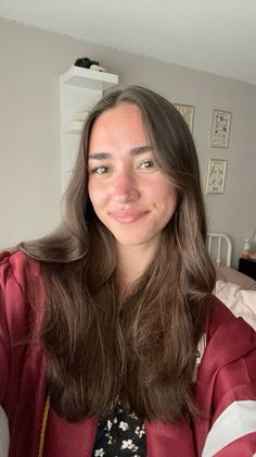 Young woman with long brown hair smiling in a graduation gown indoors