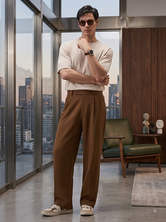 Man in brown pants and a short sleeve shirt posing indoors with a cityscape view