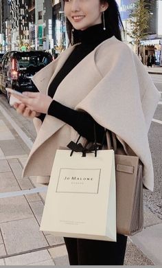 Woman holding a shopping bag and phone on a city street at night