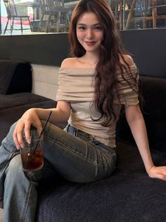 Woman with long hair wearing an off-shoulder top and jeans, sitting indoors