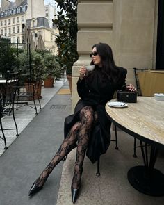 Woman in a black coat and lace tights sitting at an outdoor cafe