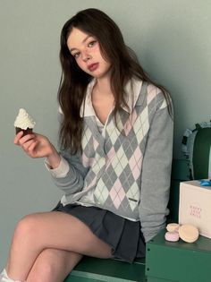 Young woman in an argyle cardigan holding a cupcake indoors