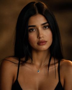 Woman with long black hair wearing a gold necklace with a blue charm