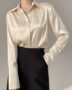 Person wearing a cream satin shirt and black pants with a silver necklace