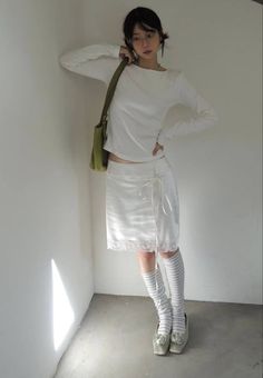 Woman in a white top and skirt with striped socks and a green bag