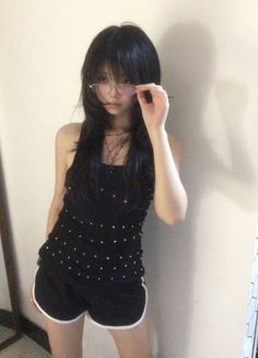 Woman with long black hair and glasses wearing a black top and shorts indoors