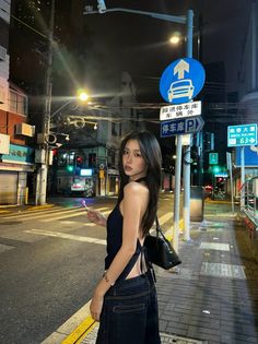 Woman in a backless top and jeans holding a lollipop on a city street at night