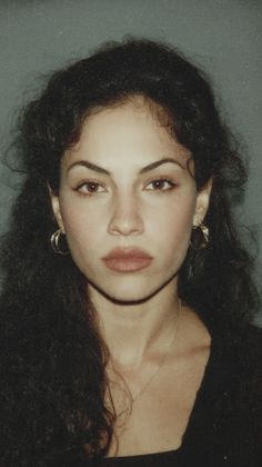 Woman with dark curly hair and hoop earrings looking directly at the camera