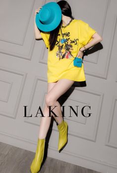 Woman in a yellow t-shirt dress and yellow boots holding a blue hat