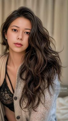 Woman with long wavy hair wearing a lace bra and cardigan indoors