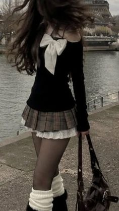 Person with long hair wearing a plaid skirt and off-shoulder top by a river