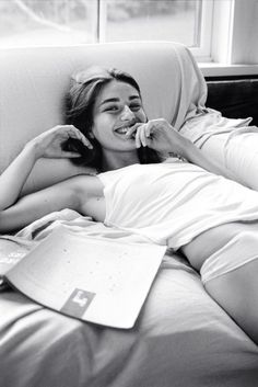 Woman in a white tank top lying on a couch, smiling at the camera