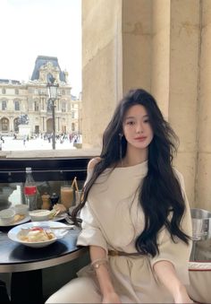 Woman with long dark hair at an outdoor cafe with a cityscape in the background