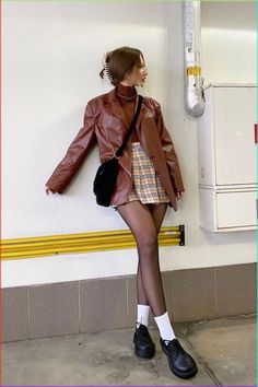 Woman in a brown leather jacket and plaid skirt with black tights and white socks