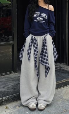 Person in an oversized sweatshirt and wide leg pants with plaid accents outdoors