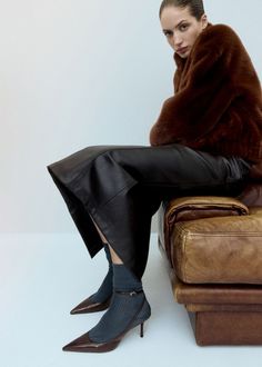 Woman in a brown fur coat and leather skirt sitting on a leather couch