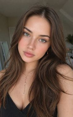Woman with long brown hair and green eyes wearing a black top and gold necklace