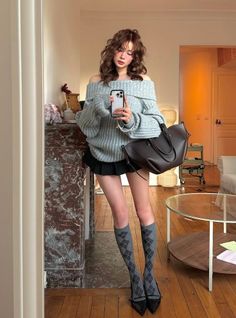 Woman in an off-shoulder sweater and pleated skirt taking a mirror selfie