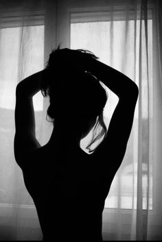 Woman in silhouette with arms raised, standing in front of a window