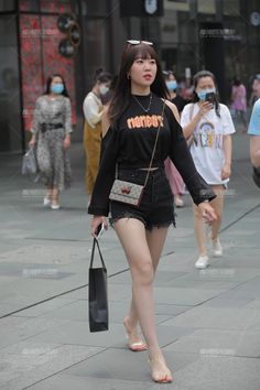 Woman in a black off-shoulder top and denim shorts walking on a street
