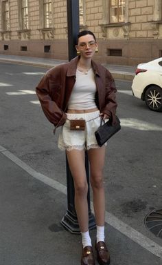 Woman in a brown leather jacket and white lace shorts on a city street