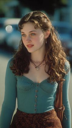 Woman with long wavy hair and blue eyes wearing a teal top and brown skirt