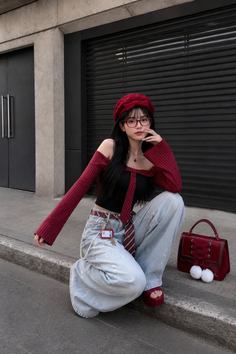 Woman in a red beret and off-shoulder top with baggy jeans crouching outdoors