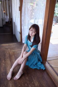 Woman in a blue checkered dress sitting on a wooden floor indoors