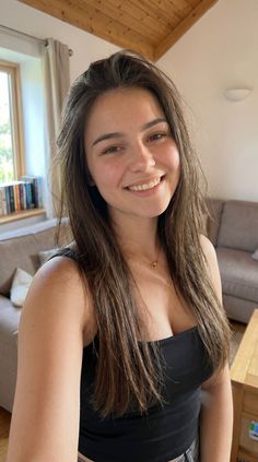 Woman with long brown hair smiling in a black top indoors