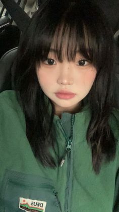 Woman with black hair and bangs wearing a green jacket indoors