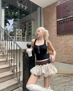 Woman with blonde hair in a black tank top and mini skirt holding a cup outdoors