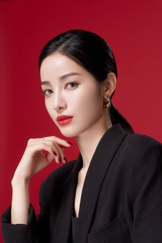 Woman with black hair and red lipstick wearing a black blazer against a red background