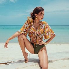 Woman in a floral top and bikini bottom with an iguana on her shoulder at the beach