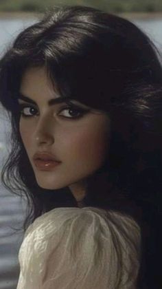 Woman with dark hair and makeup looking over her shoulder outdoors